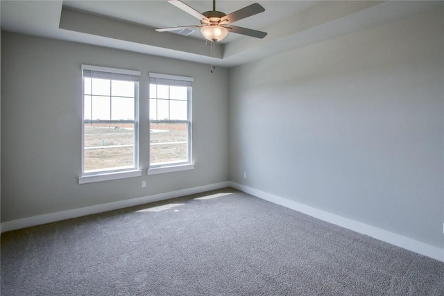 empty room with baseboards, a tray ceiling, ceiling fan, and carpet flooring