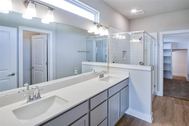 bathroom with double vanity, a stall shower, a sink, and wood finished floors