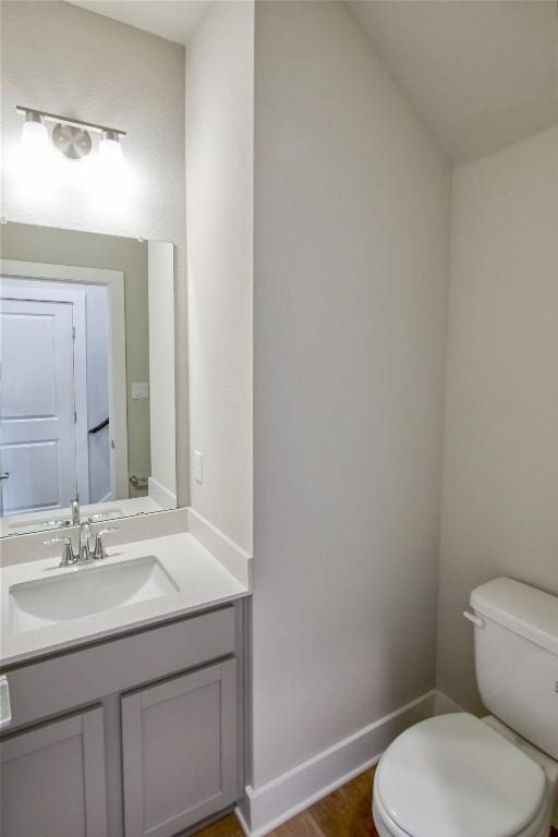 bathroom featuring toilet, baseboards, wood finished floors, and vanity