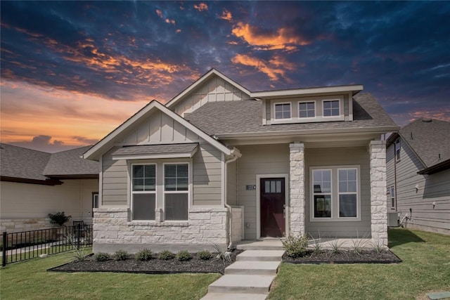 craftsman house with central AC, fence, stone siding, a lawn, and board and batten siding