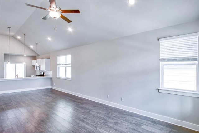 unfurnished living room featuring baseboards, a ceiling fan, dark wood finished floors, and a wealth of natural light