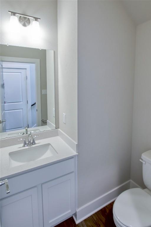 half bath with wood finished floors, vanity, toilet, and baseboards