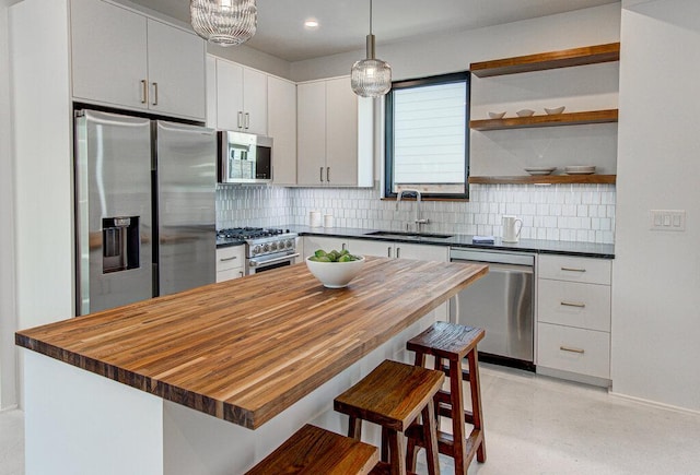 kitchen with butcher block countertops, a breakfast bar, a sink, appliances with stainless steel finishes, and tasteful backsplash