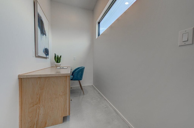 office area featuring baseboards, concrete flooring, and built in desk