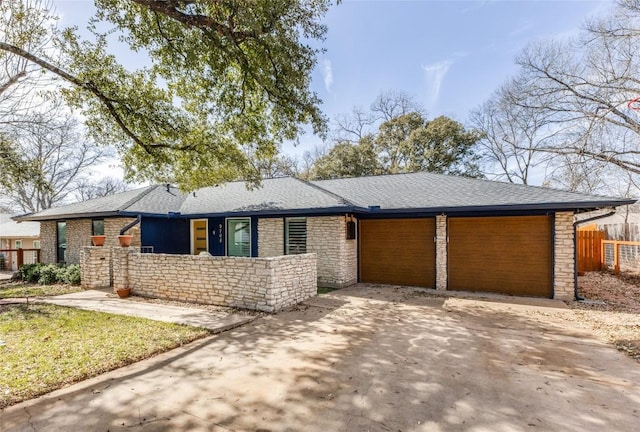 view of front facade featuring a shingled roof, fence, concrete driveway, a garage, and stone siding