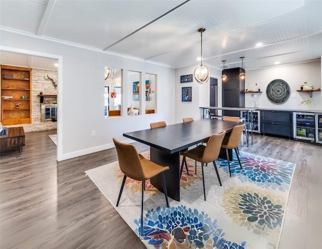 dining room with beverage cooler, wood finished floors, a stone fireplace, baseboards, and a dry bar