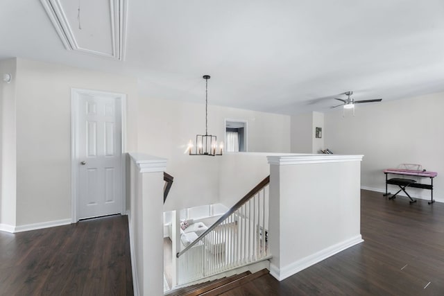 corridor featuring attic access, baseboards, dark wood-style floors, an inviting chandelier, and an upstairs landing