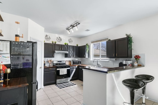 kitchen with tasteful backsplash, dark countertops, a peninsula, stainless steel appliances, and under cabinet range hood