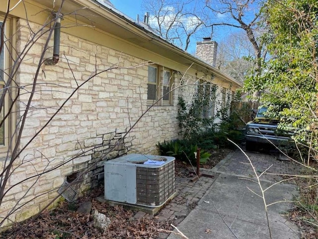 view of side of property with stone siding, a chimney, and central AC unit