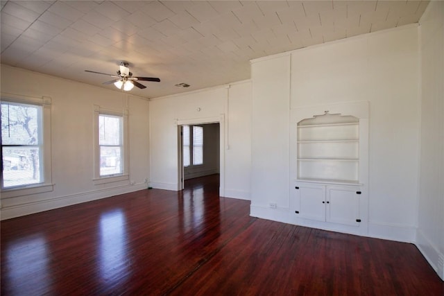 spare room featuring visible vents, baseboards, dark wood finished floors, a ceiling fan, and built in shelves