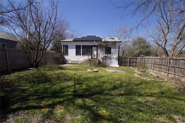 back of property with a fenced backyard, a lawn, and solar panels