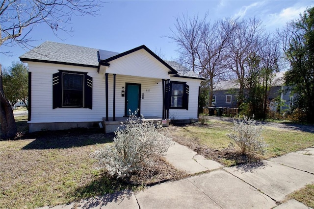 bungalow with covered porch, roof with shingles, and a front yard