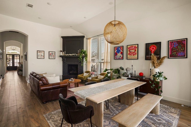 dining room with arched walkways, a fireplace, wood finished floors, visible vents, and baseboards