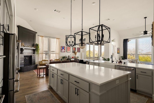 kitchen with a kitchen island, dark wood-type flooring, stainless steel appliances, a brick fireplace, and a sink