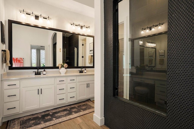 bathroom with double vanity, wood finished floors, tiled shower, and a sink