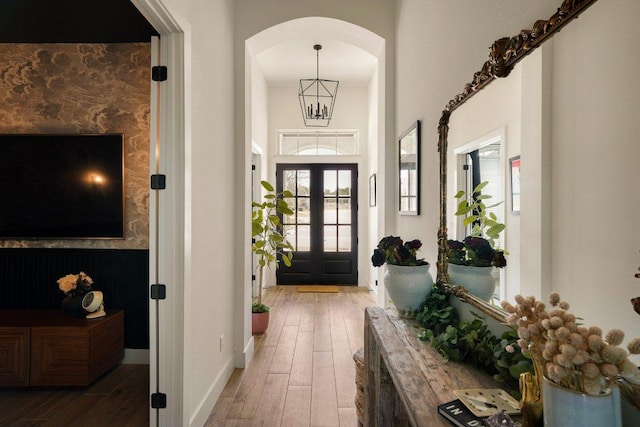 foyer entrance featuring baseboards, arched walkways, a chandelier, and wood finished floors