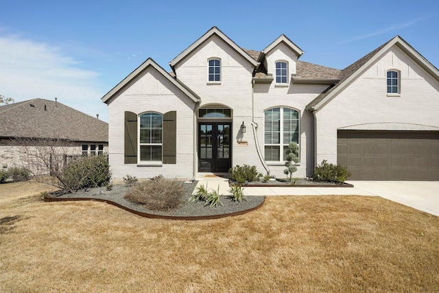 french country home with driveway, a shingled roof, an attached garage, french doors, and brick siding