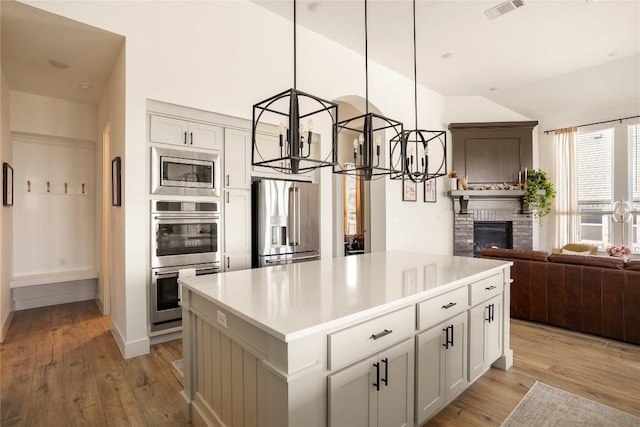 296 Running Bird Rd, Austin, TX 78737 - kitchen with light wood finished floors, a brick fireplace, appliances with stainless steel finishes, and an inviting chandelier