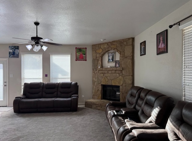 living room featuring a textured ceiling, ceiling fan, a stone fireplace, and carpet flooring