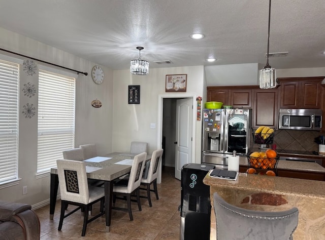 tiled dining room with a textured ceiling, a chandelier, visible vents, and baseboards