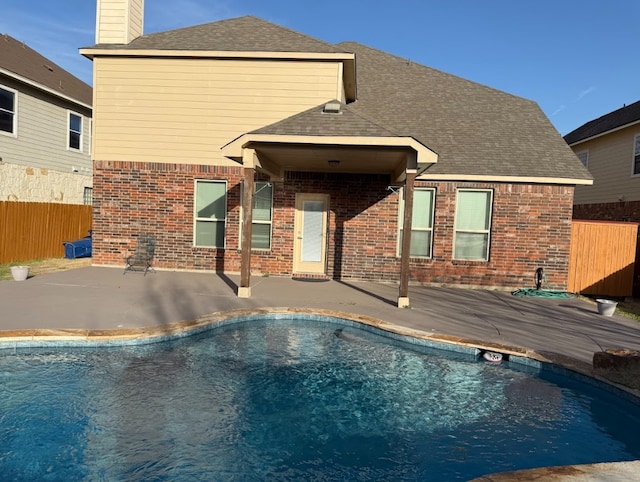 rear view of house with brick siding, a shingled roof, fence, a fenced in pool, and a patio area