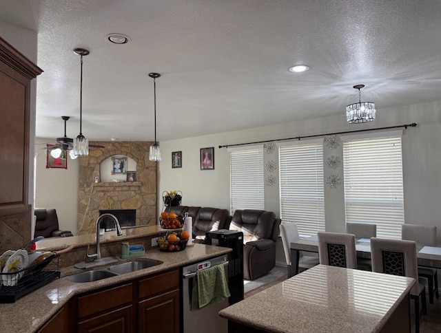 kitchen with open floor plan, a sink, a stone fireplace, pendant lighting, and stainless steel dishwasher