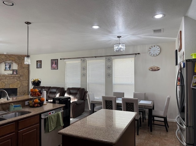 kitchen with appliances with stainless steel finishes, open floor plan, a sink, and a stone fireplace