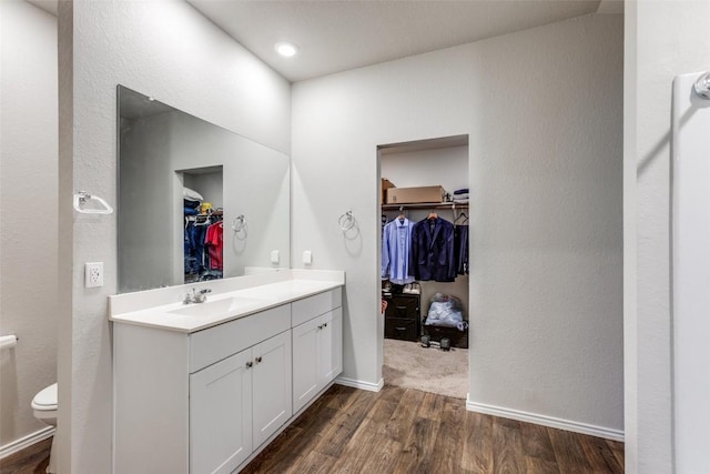 full bath with a walk in closet, toilet, vanity, wood finished floors, and baseboards