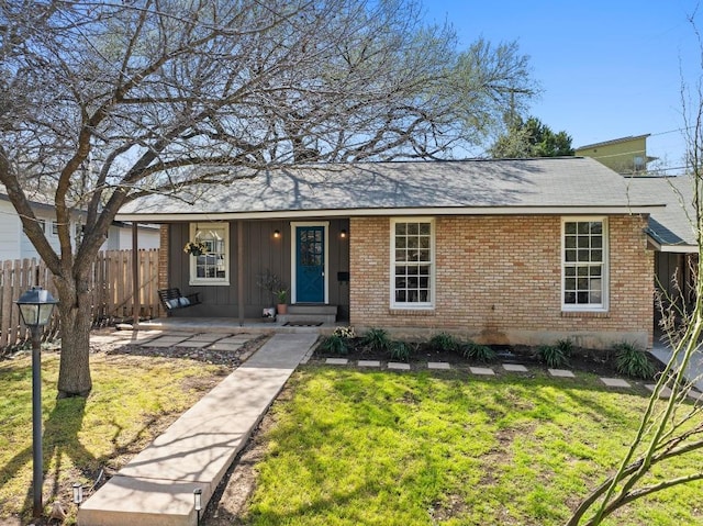 ranch-style home featuring covered porch, fence, a front yard, board and batten siding, and brick siding