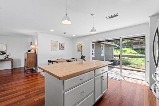 kitchen featuring butcher block countertops, visible vents, hanging light fixtures, a center island, and dark wood finished floors