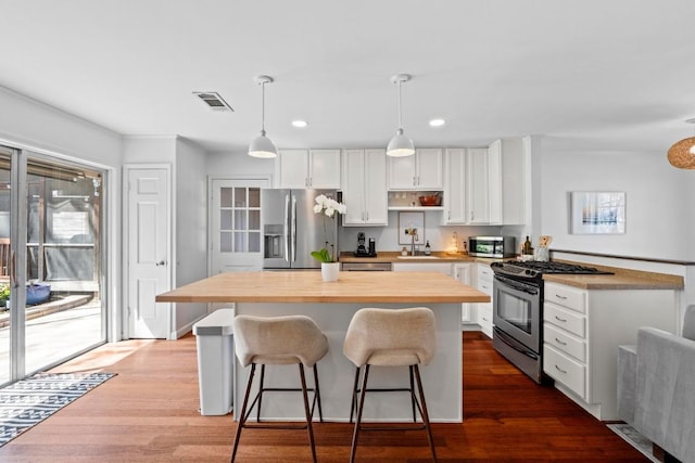 kitchen featuring stainless steel appliances, wood finished floors, wood counters, visible vents, and white cabinetry