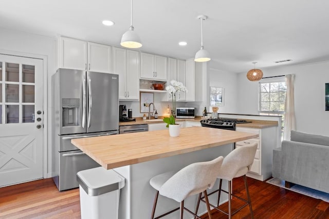 kitchen with stainless steel appliances, visible vents, a kitchen island, and wood finished floors