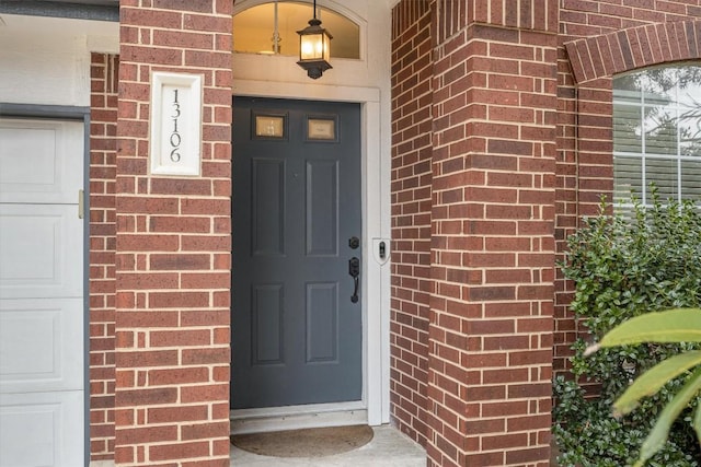 doorway to property with a garage and brick siding