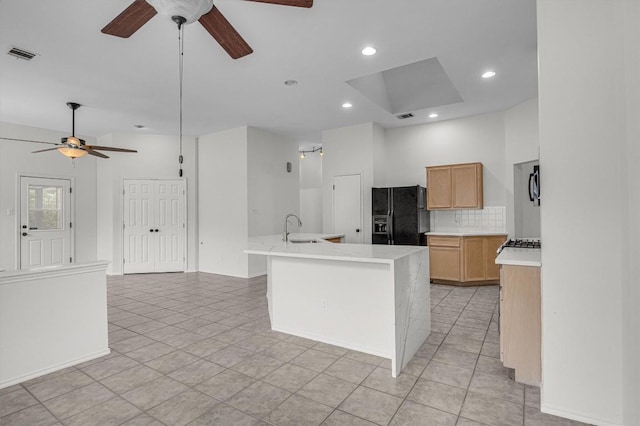 kitchen with light countertops, visible vents, black refrigerator with ice dispenser, decorative backsplash, and a sink