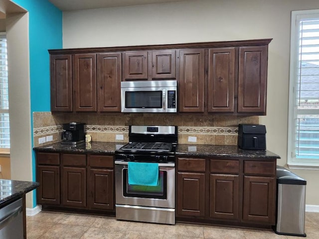 kitchen with backsplash, stainless steel appliances, dark brown cabinetry, and dark stone counters