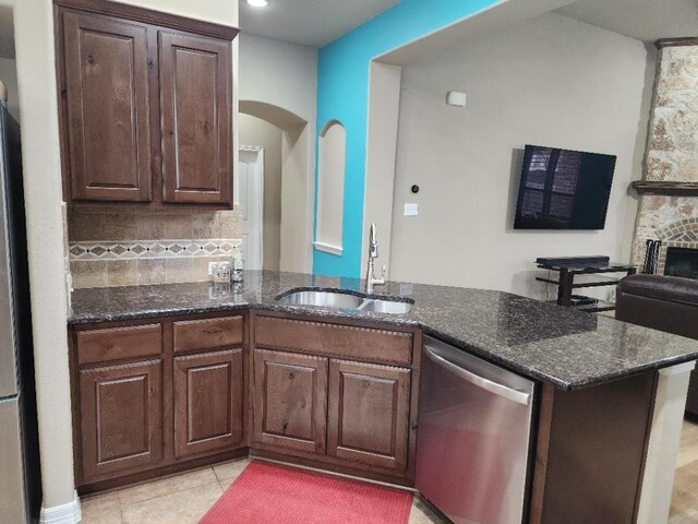 kitchen with a sink, dark stone countertops, tasteful backsplash, stainless steel dishwasher, and light tile patterned flooring