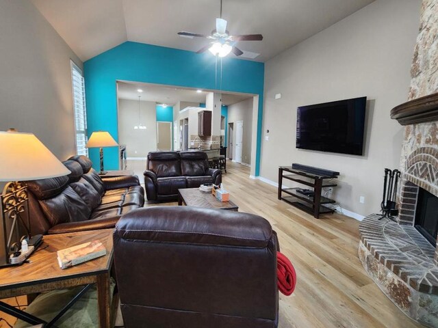 living room with a ceiling fan, baseboards, lofted ceiling, light wood-style flooring, and a fireplace with raised hearth