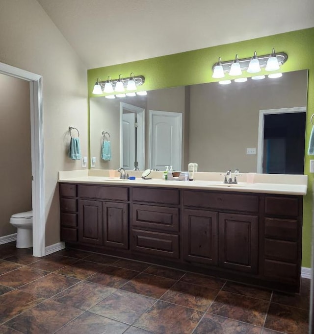 bathroom with lofted ceiling, toilet, double vanity, and a sink