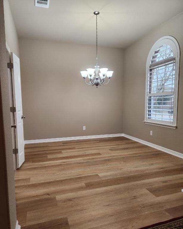 unfurnished room with an inviting chandelier, wood finished floors, and baseboards