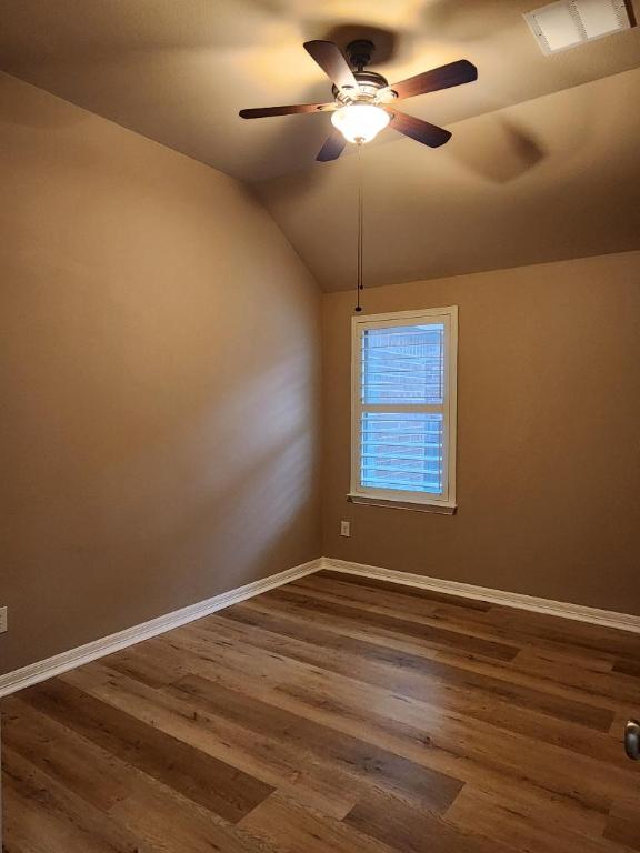 empty room featuring visible vents, baseboards, lofted ceiling, dark wood-style flooring, and ceiling fan