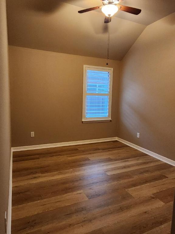 empty room with ceiling fan, baseboards, lofted ceiling, and dark wood finished floors