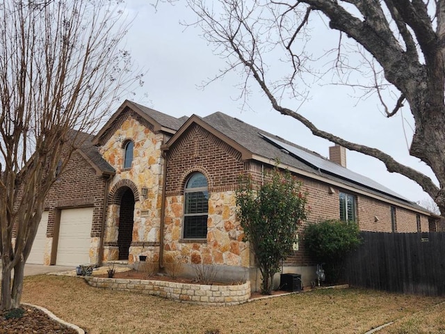 view of front of home featuring fence, a chimney, stone siding, brick siding, and roof mounted solar panels