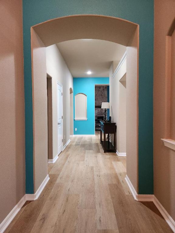 hall with light wood-type flooring, arched walkways, and baseboards