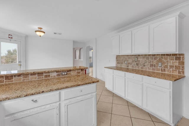 15009 Mossycup Ln, Austin, TX 78724 - kitchen featuring arched walkways, tasteful backsplash, light stone countertops, and white cabinetry