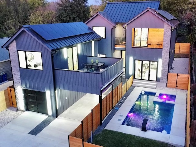 rear view of property featuring metal roof, a balcony, fence, a fenced in pool, and a standing seam roof