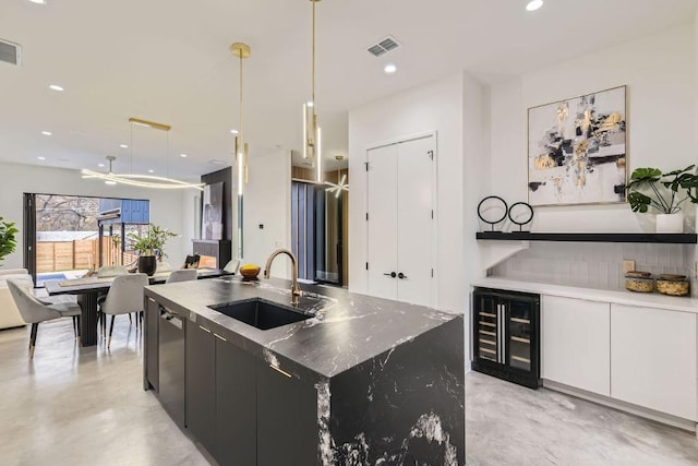 kitchen featuring visible vents, a sink, an island with sink, modern cabinets, and beverage cooler