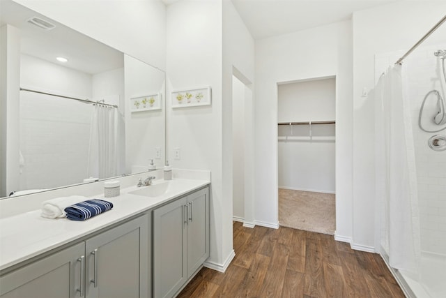 full bathroom featuring a tile shower, wood finished floors, vanity, and baseboards