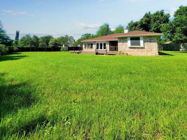 back of property featuring a lawn, a chimney, fence, a wooden deck, and brick siding