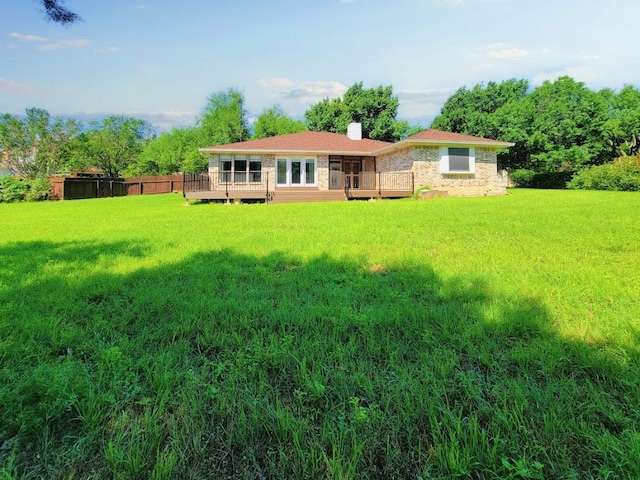 rear view of property featuring a yard, a chimney, a wooden deck, and fence