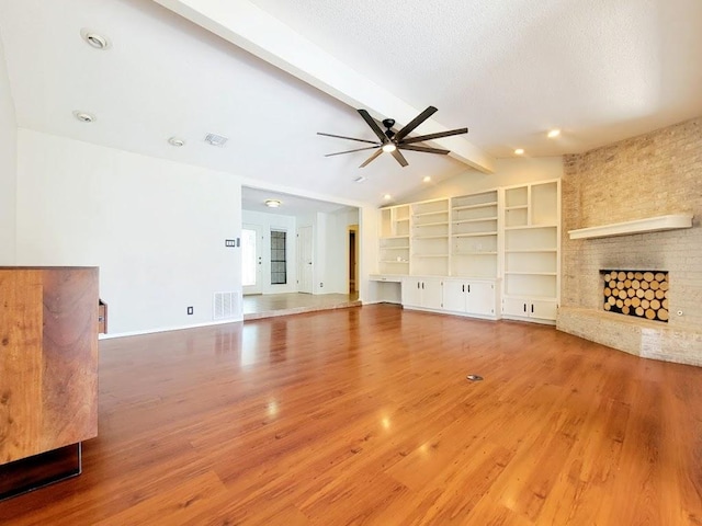 unfurnished living room featuring lofted ceiling with beams, ceiling fan, a textured ceiling, a fireplace, and wood finished floors